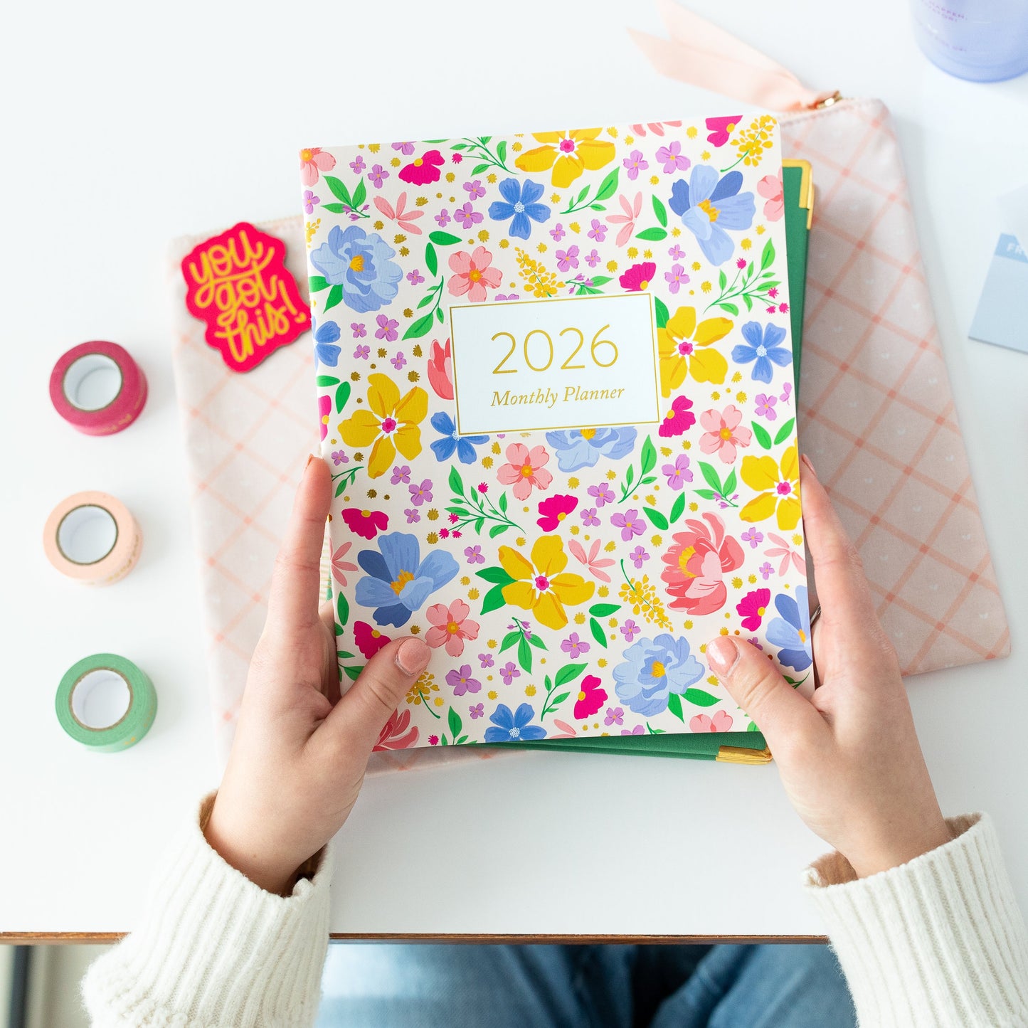 Person holding a colorful 2026 planner on a desk with stationery items.
