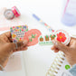 Hands holding stickers with a planner and stationery items in the background