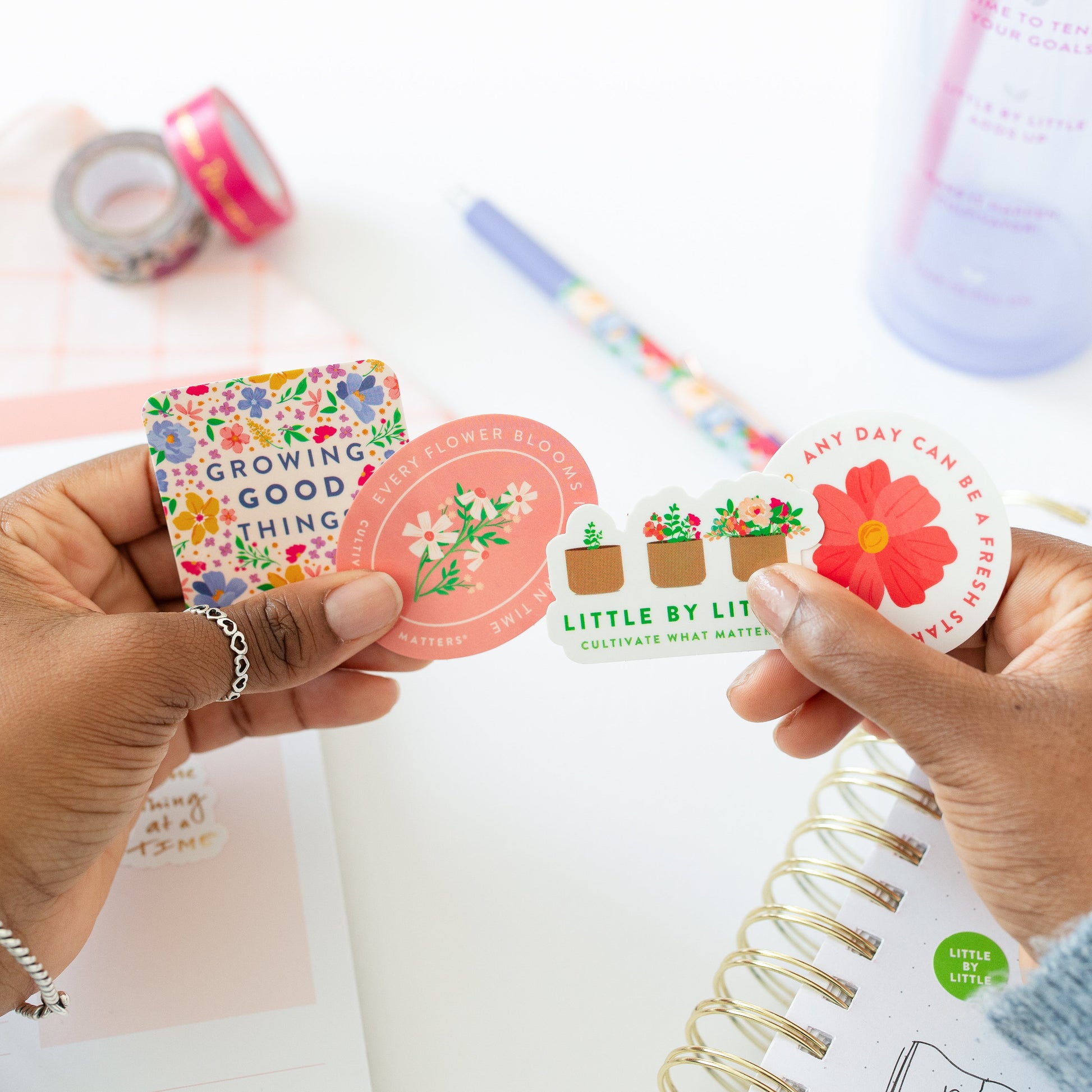 Hands holding stickers with a planner and stationery items in the background
